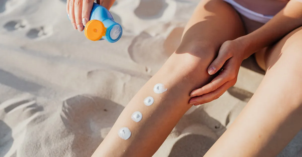 Close-up of applying sunscreen on legs at the beach for skin protection.