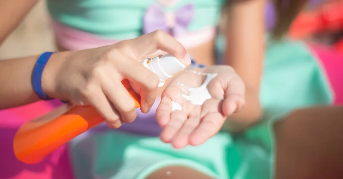 Young girl applying sunscreen from spray bottle outdoors. Summer protection.